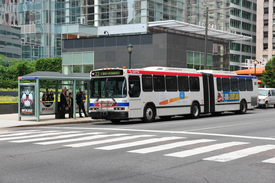 A bus stop in Philadelphia, where people wait under a glass shelter for a bus as it arrives.